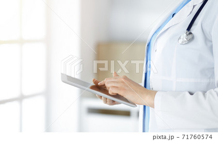 Unknown woman-doctor standing in sunny clinic and using tablet pc, close-up. Data and best service in medicine 71760574
