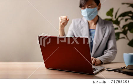 Small Business and Successful during Coronavirus Concept. blurred Gladful Business Woman wearing Mask, Working on Laptop in Office. Focus on Computer. Business Achieves Goals. Celebrating Success 71762103
