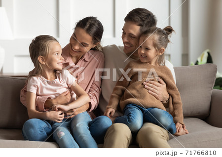Little daughters sit on parents laps talking resting on couch 71766810