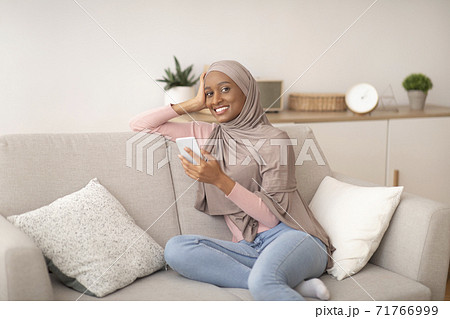 Young black woman in hijab using smartphone for work or studies on sofa at home Young black woman in hijab using smartphone for work or studies on sofa at home 71766999