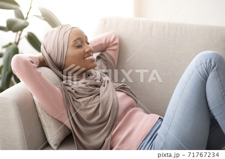 Lovely black lady in hijab lying on sofa, closing her eyes and smiling, taking nap at midday, indoors Lovely black lady in hijab lying on sofa, closing her eyes and smiling, taking nap at midday, indoors 71767234