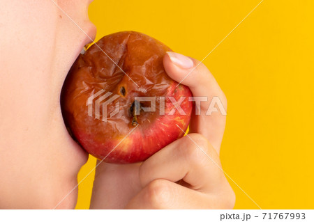 The girl bites a rotten apple with a worm on a yellow background. Expired products, junk food 71767993