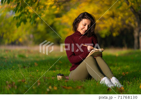 A person write notes sitting on a lawn in an autumn park. Joyful state of mind. Looking for inspiration A person write notes sitting on a lawn in an autumn park. Joyful state of mind. Looking for inspiration 71768130
