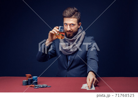 Stylish bearded Man in suit and scarf playing in dark casino, smoking cigar, drink whiskey Stylish bearded Man in suit and scarf playing in dark casino, smoking cigar, drink whiskey 71768525