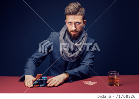 Stylish bearded Man in suit and scarf playing in dark casino, smoking cigar, drink whiskey Stylish bearded Man in suit and scarf playing in dark casino, smoking cigar, drink whiskey 71768526