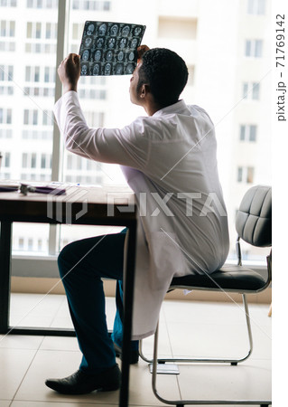 African American black man doctor looking at MRI brain scan image while working at desk with laptop 71769142