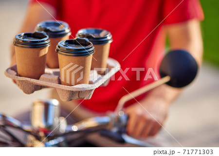 Male courier holding four coffee cups, delivering order by scooter to customer Male courier holding four coffee cups, delivering order by scooter to customer 71771303