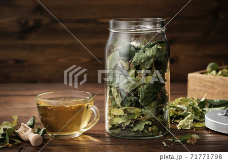 Cup of healthy tea with Linden tree flowers, jar of dry flowers and leaves of lime or Tilia cordata tree. Treatment for cold and flu. 71773798