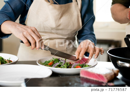 Hands of mature female putting slice of smoked meat on plate with salad 71776587