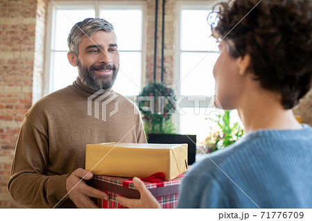 Happy bearded man passing two gifts to his wife while looking at her with smile 71776709