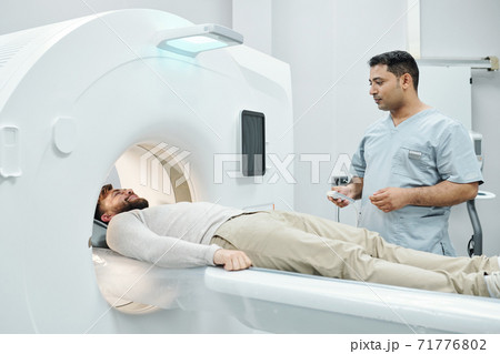 Young mixed-race male doctor in medical uniform touching button on control panel 71776802