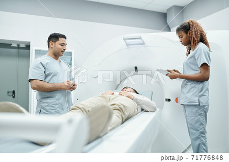Young nurse or assistant in uniform making notes while standing by couchette Young nurse or assistant in uniform making notes while standing by couchette 71776848