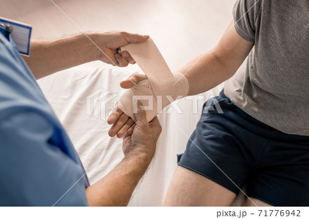 Hands of clinician wrapping palm and wrist of sick patient with flexible bandage 71776942