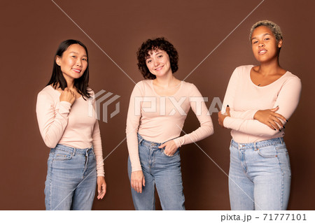 Young joyful women in white pullovers and blue jeans standing in front of camera 71777101