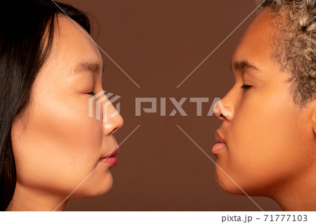 Side view of faces of two young intercultural women standing in front of camera Side view of faces of two young intercultural women standing in front of camera 71777103