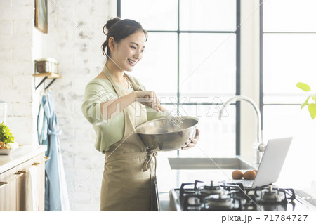 パソコンを見ながら料理を作る女性 パソコンを見ながら料理を作る女性 71784727