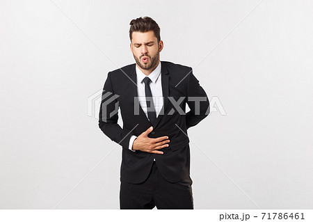 Unhappy man with stomach pain spasm. portrait of handsome bearded businessman in suit. Indoor studio shot, isolated on grey background 71786461