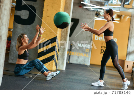Partner workout. Two young athletic women in sportswear exercising with ball at gym 71788146