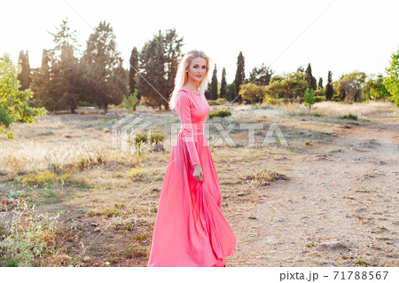 Beautiful blonde woman in pink dress walks in the park at sunset Beautiful blonde woman in pink dress walks in the park at sunset 71788567