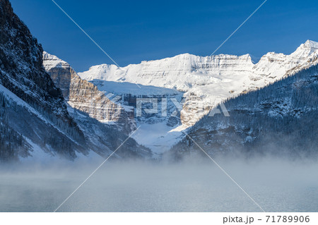 Lake Louise in early winter sunny day morning. Mist floating on turquoise color water surface. Clear blue sky, snow capped mountains in background. Beautiful natural landscape in Banff National Park. Lake Louise in early winter sunny day morning. Mist floating on turquoise color water surface. Clear blue sky, snow capped mountains in background. Beautiful natural landscape in Banff National Park. 71789906