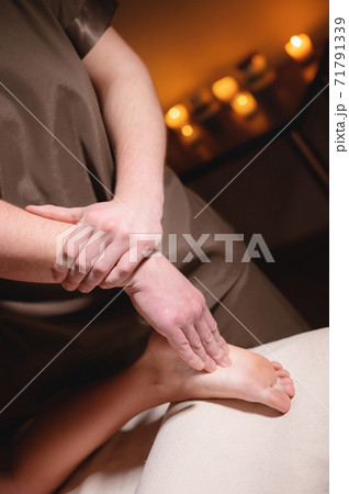 Professional massage of female feet by a man masseur in a dark spa salon with candles 71791339