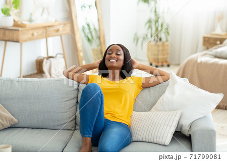 Happy black woman relaxing on cozy sofa at home, having peaceful time on weekend morning Happy black woman relaxing on cozy sofa at home, having peaceful time on weekend morning 71799081