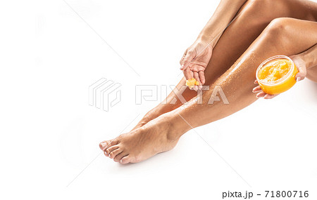 Young woman applying natural fruit scrub on her legs. Young woman applying natural fruit scrub on her legs. 71800716