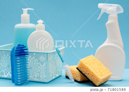 Bottles of dishwashing liquid in basket, sponges and brushes on blue background. Bottles of dishwashing liquid in basket, sponges and brushes on blue background. 71801589