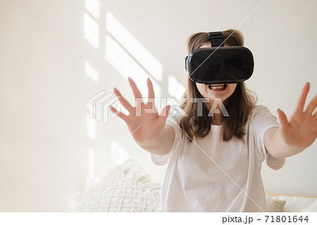 Young woman in jeans and white T-shirt with virtual reality glasses on her head moves her arms, dances, gets scared. The concept of modern technology, VR, virtual games, entertainment. 71801644