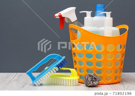 Bottles of dishwashing liquid, brushes and sponge in a basket on wooden desk. Bottles of dishwashing liquid, brushes and sponge in a basket on wooden desk. 71802196
