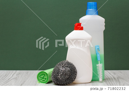 Bottles of dishwashing liquid, brush, garbage bags and sponge on green background. 71802232