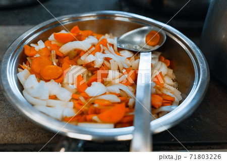 Carrots and onions are stewed in a large shiny plate on the stove. Vegetables are prepared for eating. Carrots and onions are stewed in a large shiny plate on the stove. Vegetables are prepared for eating. 71803226