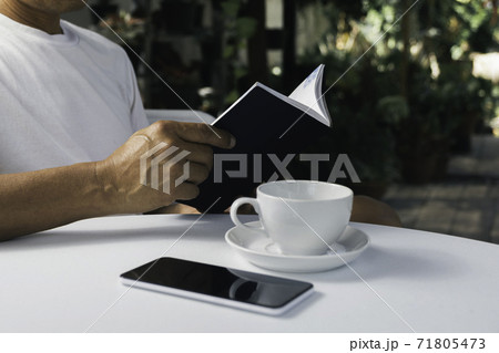 A man reading a book with coffee cup. Man sitting in chair at home, reading book and relaxing. 71805473