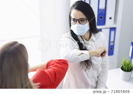 Two women in medical protective masks greet each other in office. Two women in medical protective masks greet each other in office. 71805809