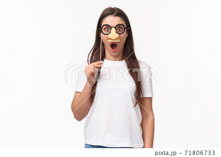 Entertainment, fun and holidays concept. Funny and cute young girl fool around, praying wearing glasses and nose mask, gasping amazed, look surprised standing white background Entertainment, fun and holidays concept. Funny and cute young girl fool around, praying wearing glasses and nose mask, gasping amazed, look surprised standing white background 71806733