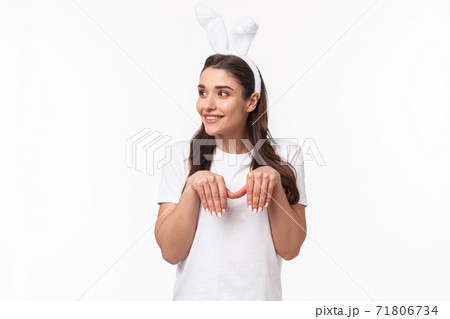 Portrait of funny and cute, playful adult girl in t-shirt and rabbit ears, look away with amused happy face, imitating bunny with paws and silly grin, look away, standing white background Portrait of funny and cute, playful adult girl in t-shirt and rabbit ears, look away with amused happy face, imitating bunny with paws and silly grin, look away, standing white background 71806734