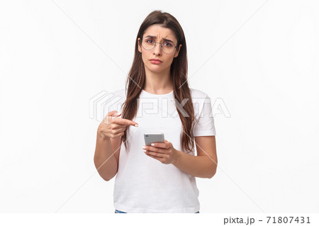 Communication, technology and lifestyle concept. Waist-up potrait of sad and gloomy young uneasy caucasian woman in glasses, frowning and pointing at mobile phone with regret or sadness 71807431
