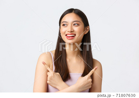 Beauty, fashion and people emotions concept. Dreamy happy beautiful asian woman in dress, smiling and lick lips from temptation, pointing fingers sideways two choices, white background Beauty, fashion and people emotions concept. Dreamy happy beautiful asian woman in dress, smiling and lick lips from temptation, pointing fingers sideways two choices, white background 71807630