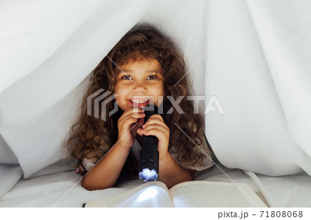 Little girl reads a book at night with a flashlight under a blanket 71808068