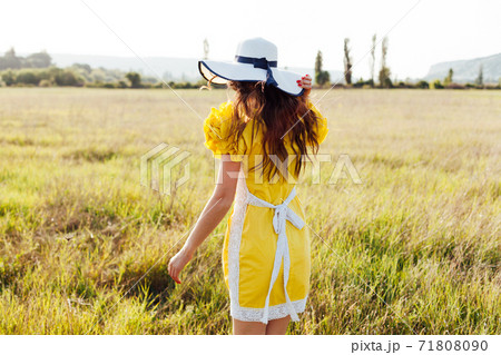 beautiful woman in a yellow dress and hat walks around the field at sunset 71808090