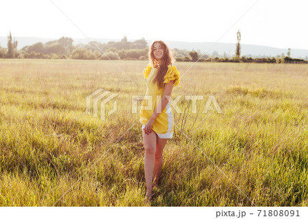 Beautiful woman in yellow dress walks on the field at sunset 71808091