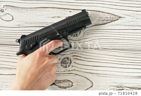 Man hand holding black modern metal gun on white wooden table, closeup detail 71810428