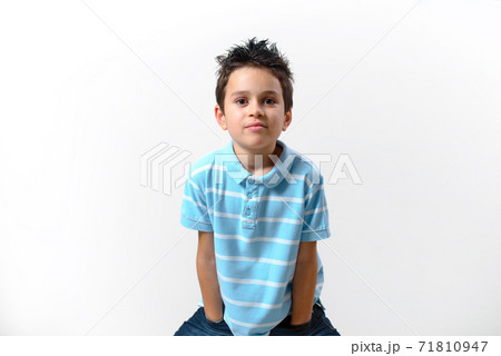A boy in a blue T-shirt stands with his hands in his pockets bent over and looks straight into the camera. A boy in a blue T-shirt stands with his hands in his pockets bent over and looks straight into the camera. 71810947