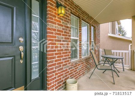 Front porch of a home with table and chairs in front of brick wall and window 71813517