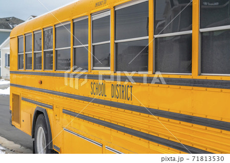 Close up of a yellow school bus on a snowy road against homes and cloudy sky Close up of a yellow school bus on a snowy road against homes and cloudy sky 71813530