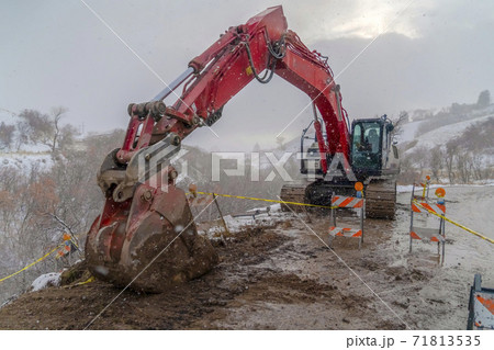 Excavator on a muddy road with barricades and yellow tape viewed in winter 71813535