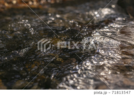 Close up of a stream with translucent frozen water over dark rocks Close up of a stream with translucent frozen water over dark rocks 71813547