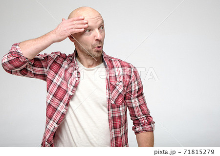 Funny, shocked bald man, with a bizarre expression on face, holds hand near head and looks surprised 71815279