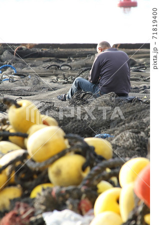 岸壁に広げた漁網を手入れする男性 71819400