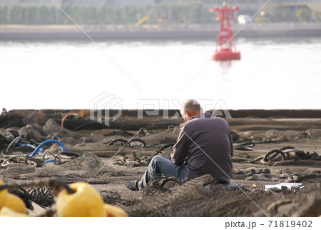 岸壁に広げた漁網を手入れする男性 71819402